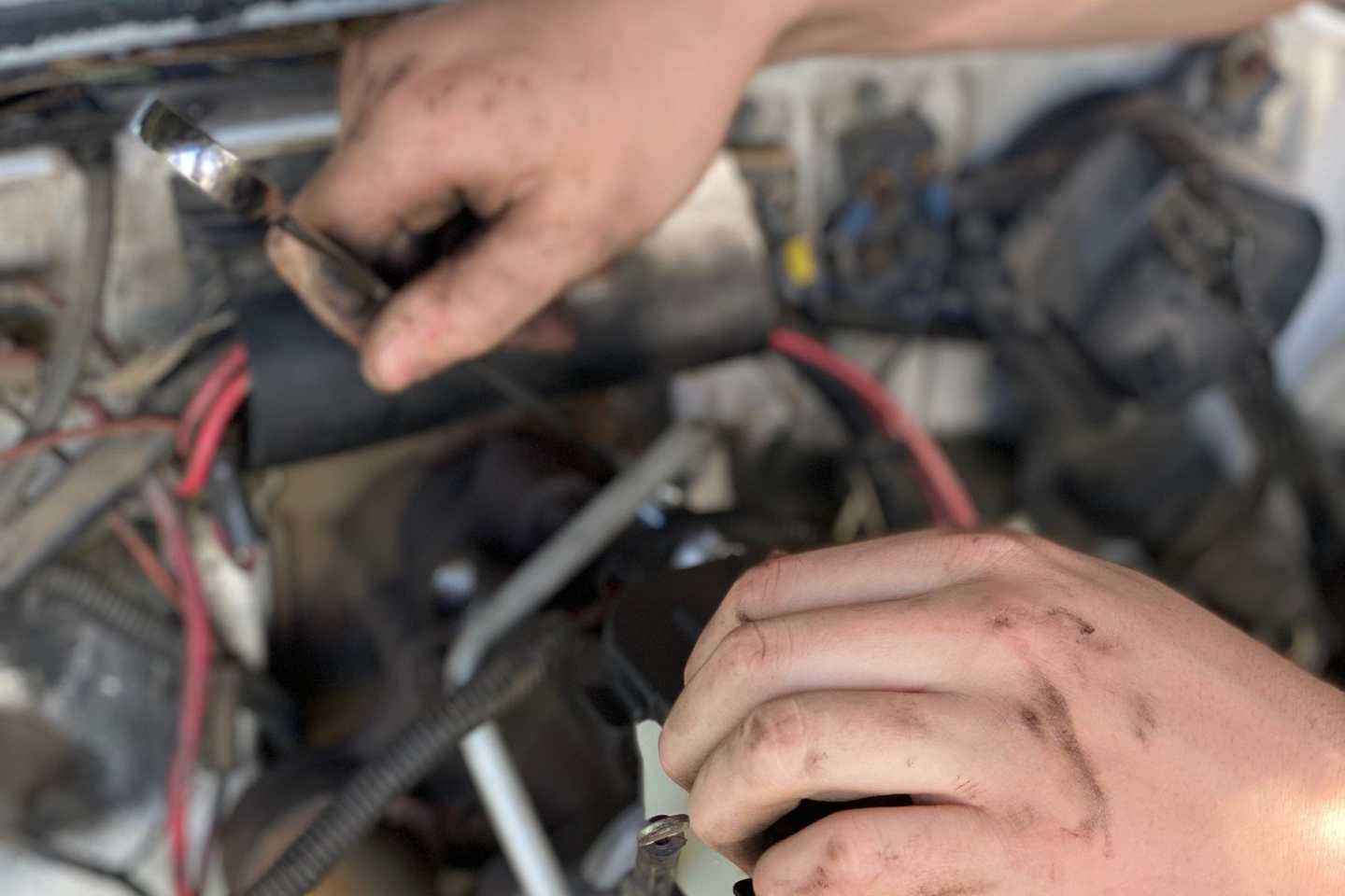 Zwei ölverschmierte Hände arbeiten im geöffneten Motorraum
