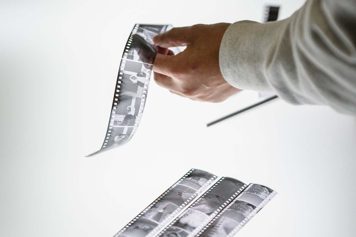 Eine Hand hält einen Filmstreifen hoch, weitere Streifen liegen auf einer hellen Fläche