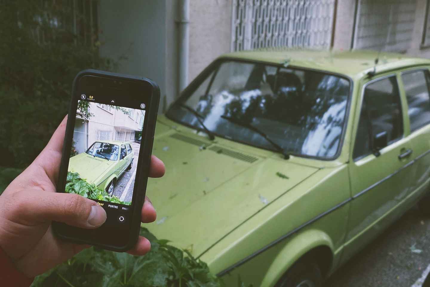 Eine Hand hält ein Smartphone vor einen hellgrünen Kleinwagen; auf dem Display ist derselbe Wagen zu sehen