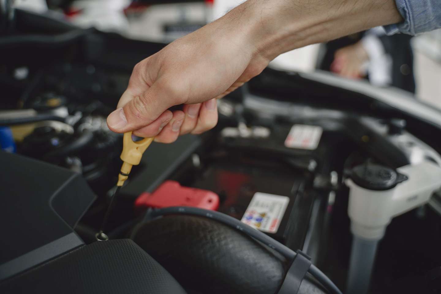 Eine Hand zieht den Ölmessstab aus dem geöffneten Motorraum eines Fahrzeugs