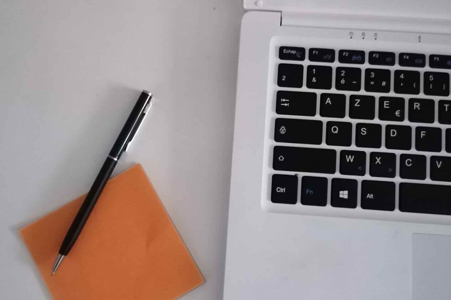 Schwarzer Stift auf einem orangefarbenen Notizzettel neben einer Laptoptastatur