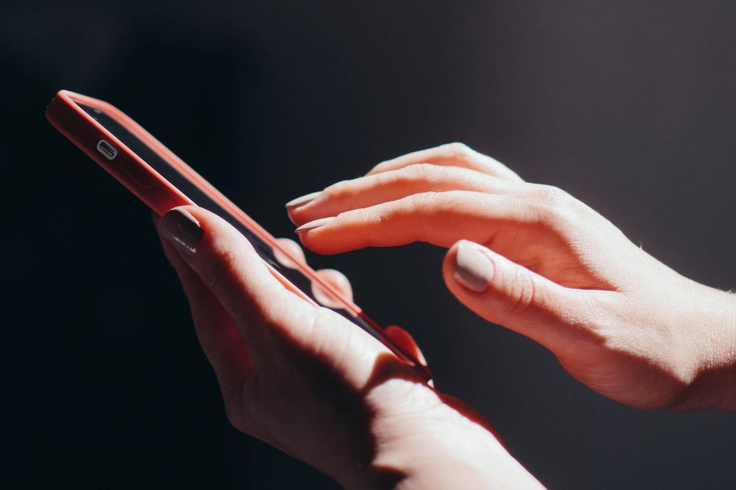 Zwei Hände halten ein Smartphone vor dunklem Hintergrund