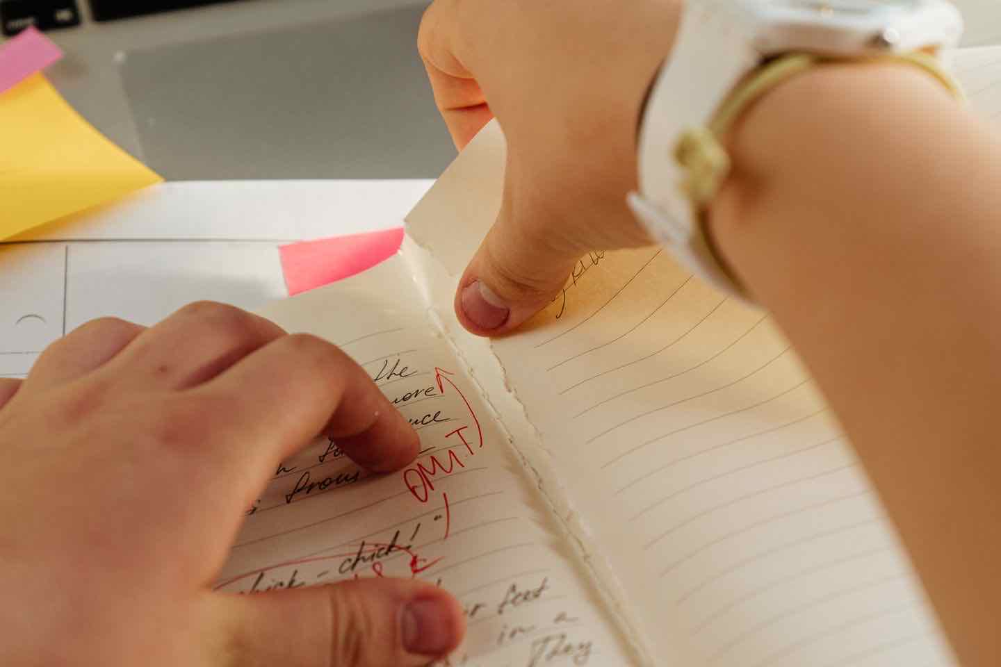 Hände über einem handschriftlich beschriebenen Notizbuch mit roten Anmerkungen