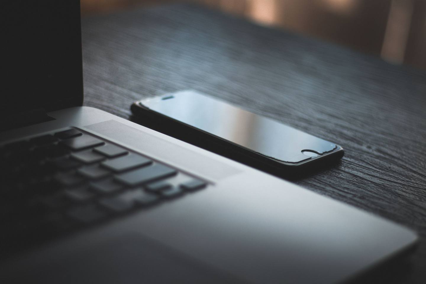 Laptop und Smartphone nebeneinander auf einem dunklen Holztisch