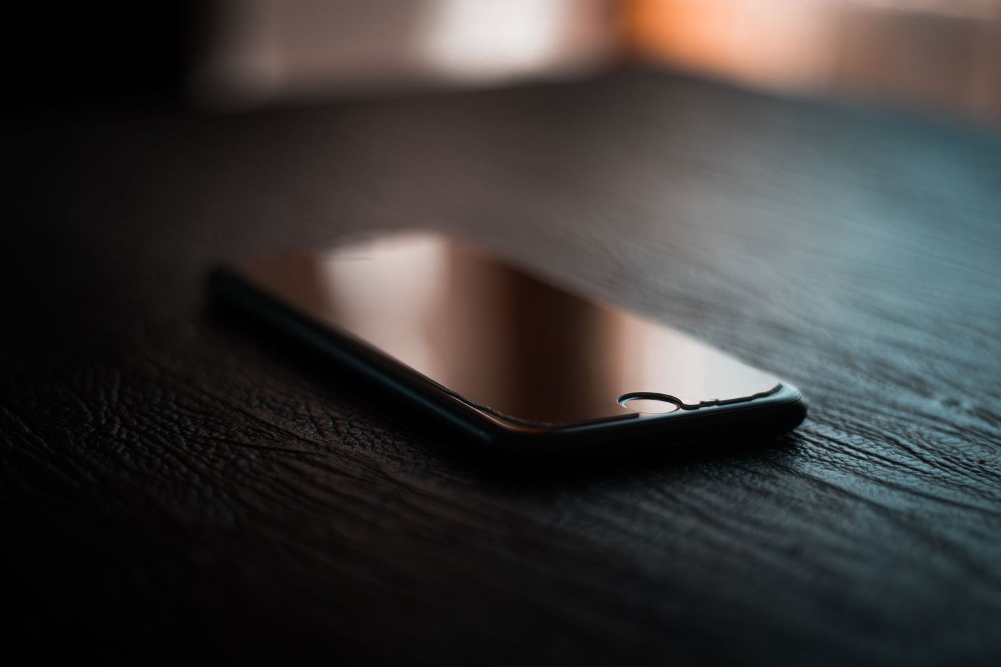 Smartphone mit ausgeschaltetem Bildschirm liegt auf einem dunklen Holztisch