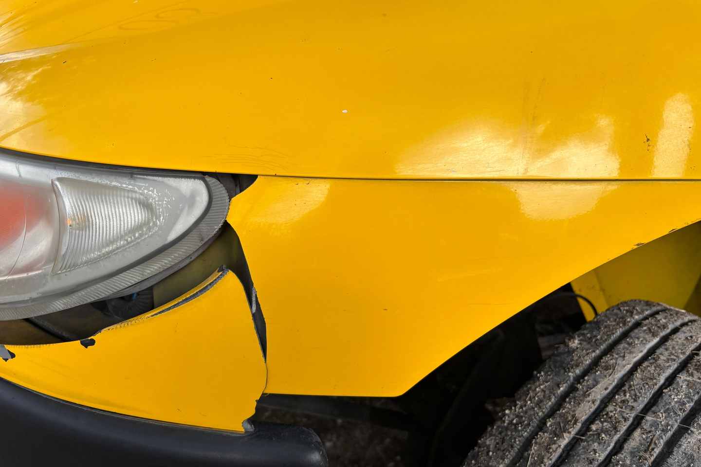 Delle und Schramme am vorderen Kotflügel eines gelben Fahrzeugs neben dem Scheinwerfer